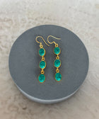 Front Facing Shot of Zara Gold Plated Sterling Silver with 3 Chain Linked Turquoise Gems Earrings on Soft Pillow